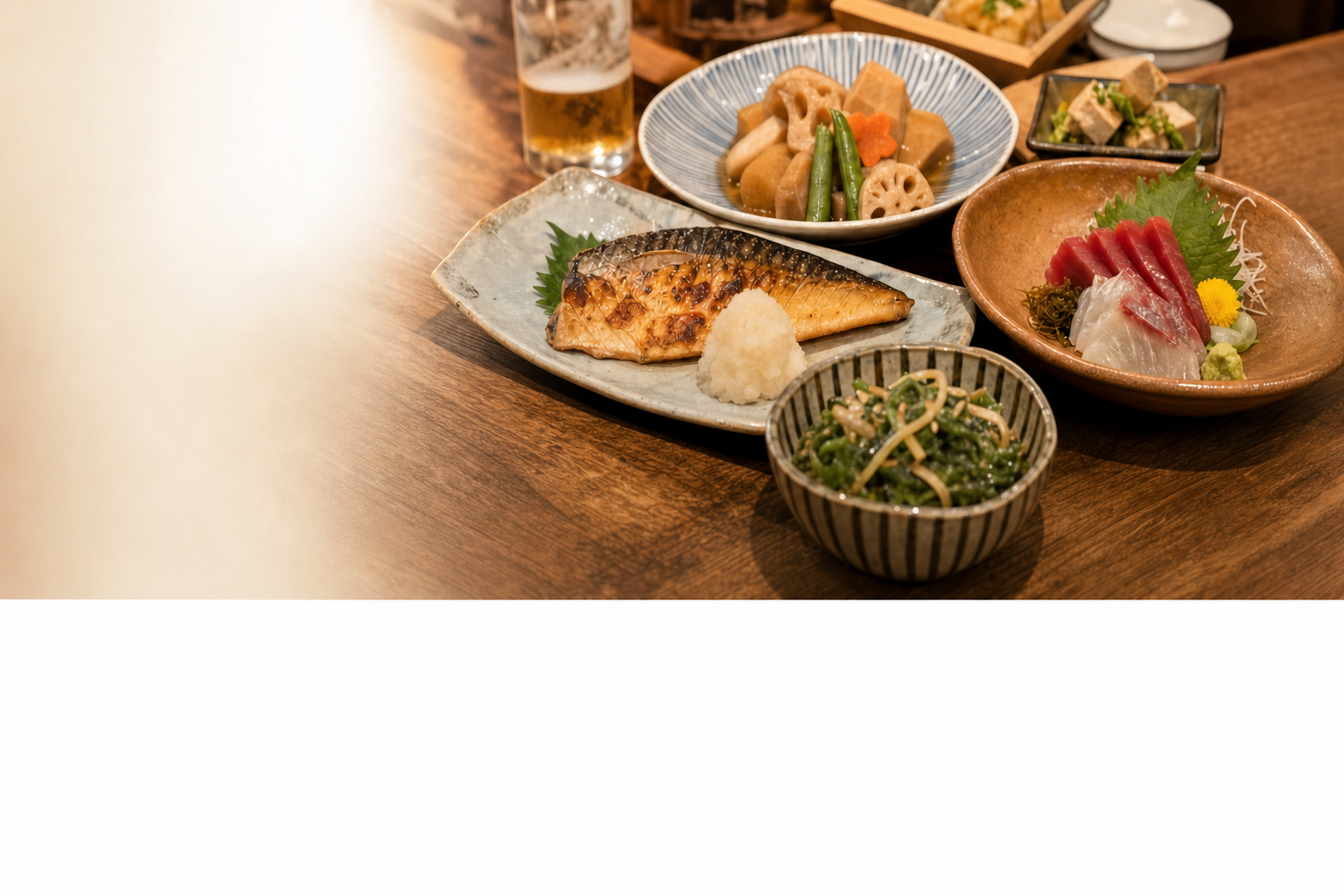 焼き魚や煮物、刺身など季節の和食が木の卓に並ぶ様子